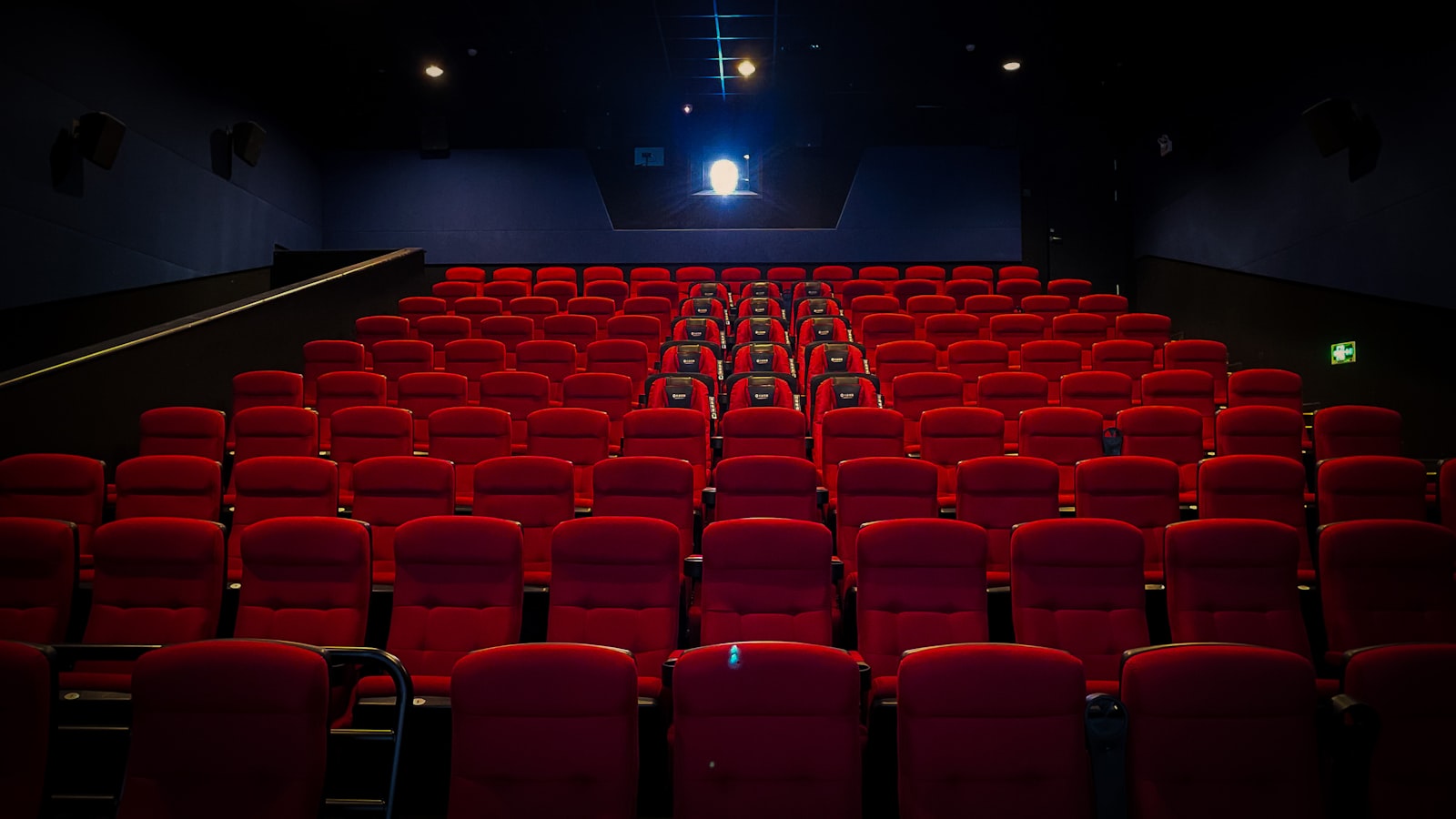 Rows of red seats in a dark auditorium, lit only by the port window at the back of the room.