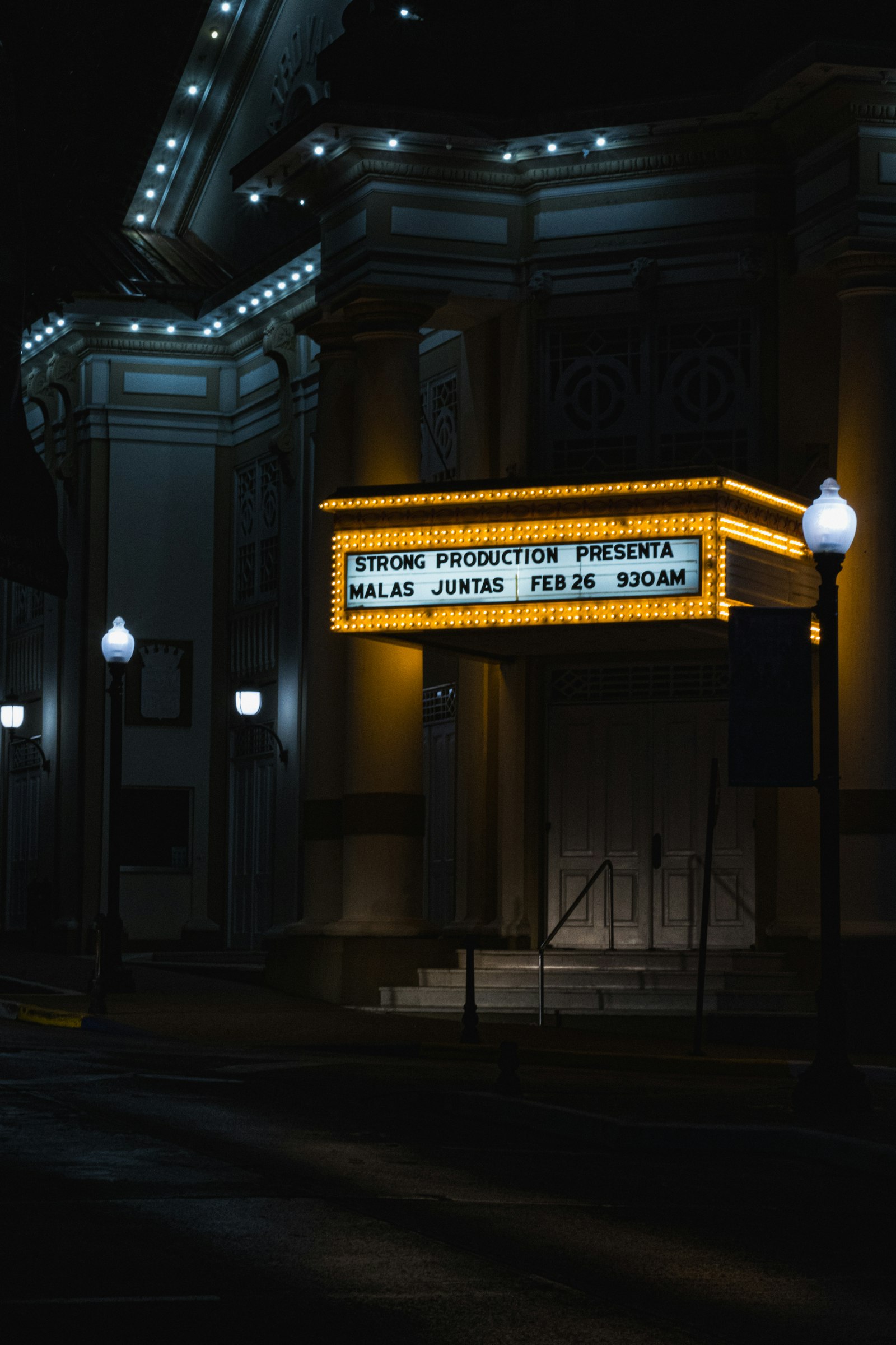 A theatre marquee lit in warm amber against a black street, the bulbs running around its edge.