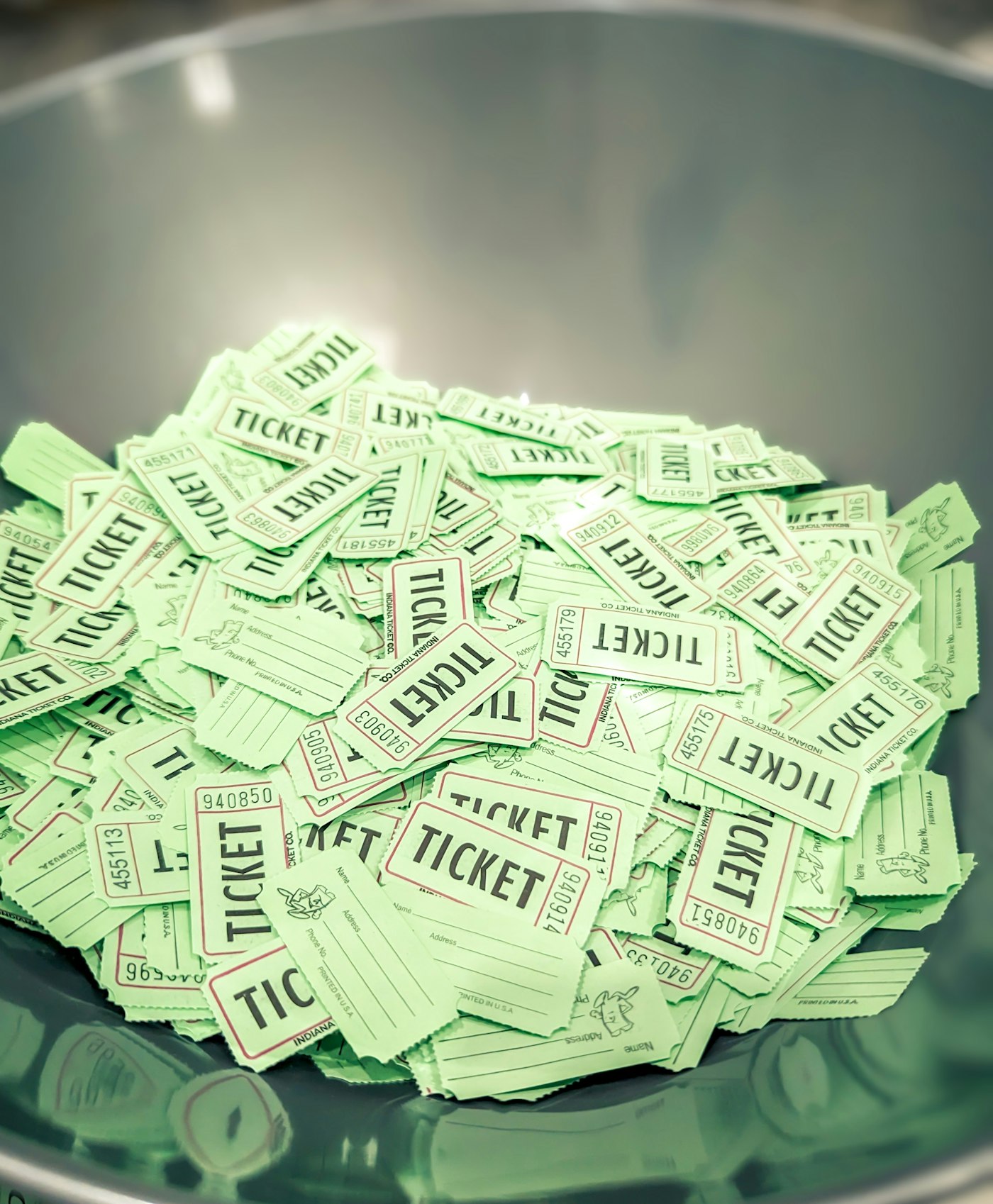 A steel bowl heaped with green paper roll tickets, each stamped with a serial number.